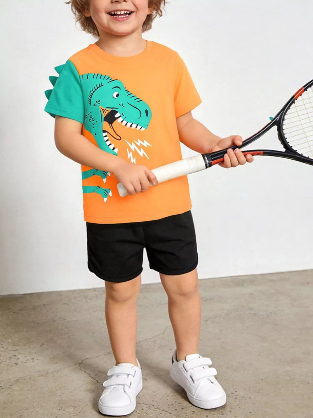 Toddler boys' orange cotton tee with roaring dinosaur graphic and teal sleeves, paired with black shorts.
