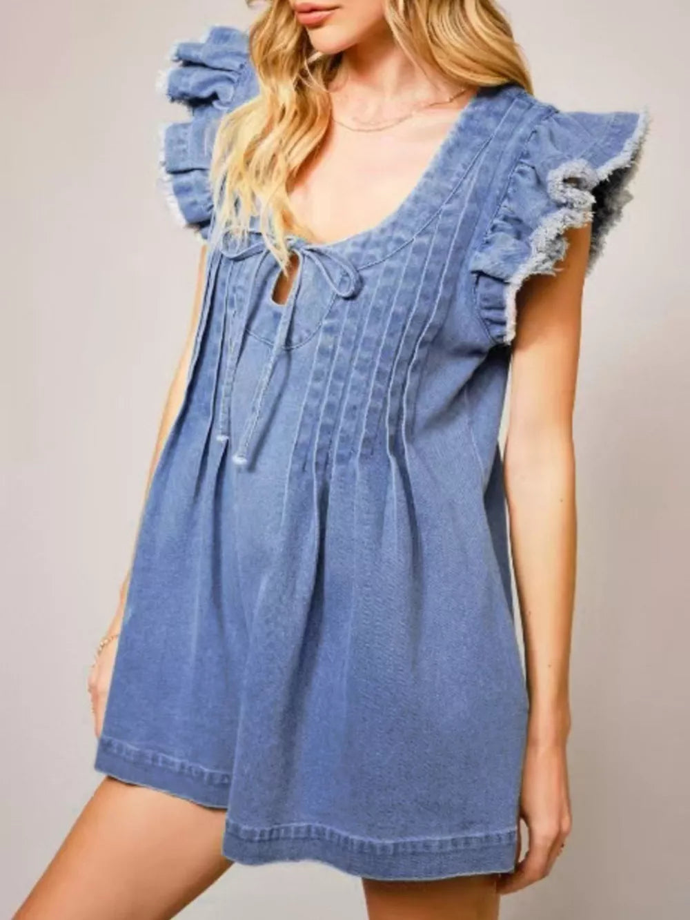 Denim romper with ruffled sleeves, tie neckline, and pintuck details.
