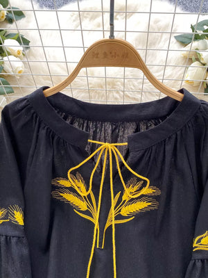 Black tie-neck blouse with yellow wheat embroidery and bell sleeves.