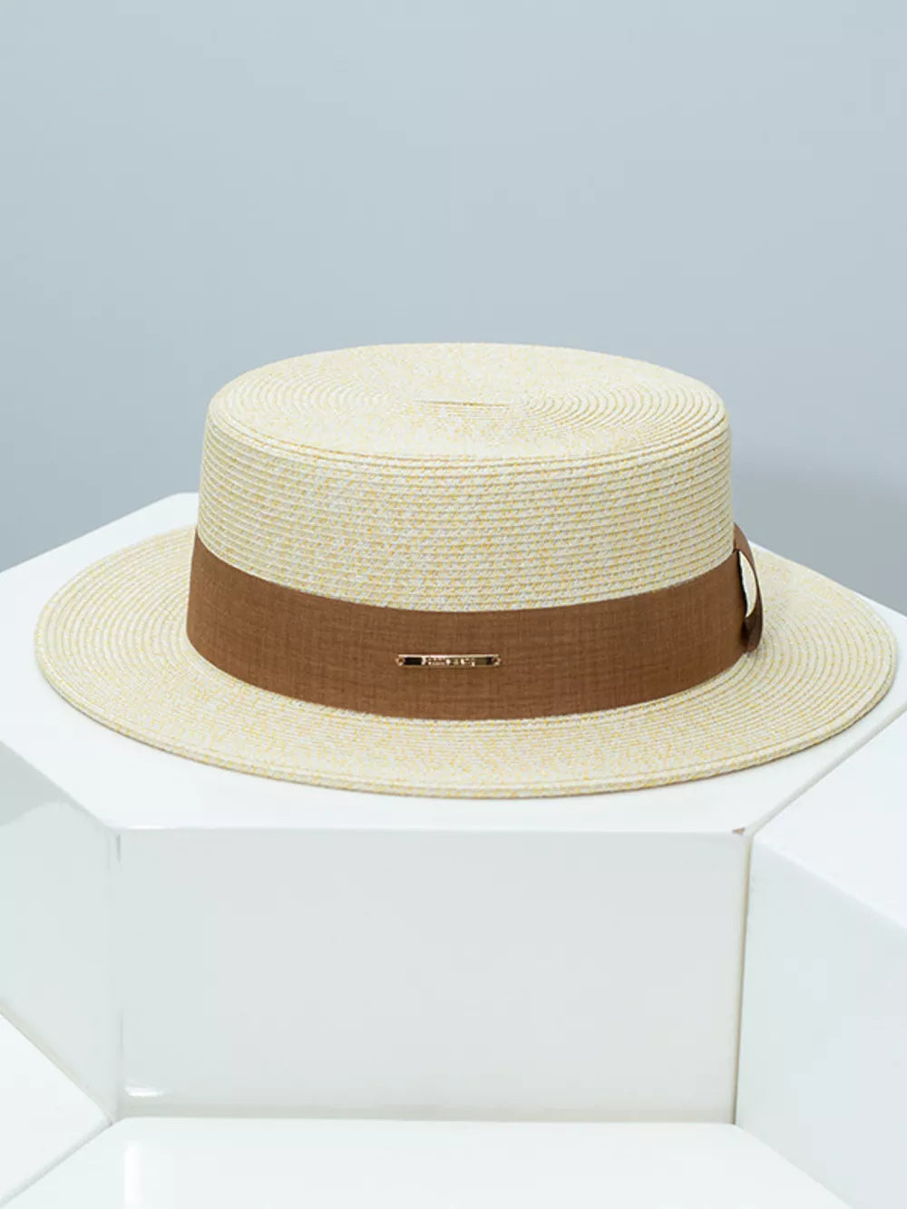 Elegant straw boater hat in beige with a brown ribbon band and gold detail.