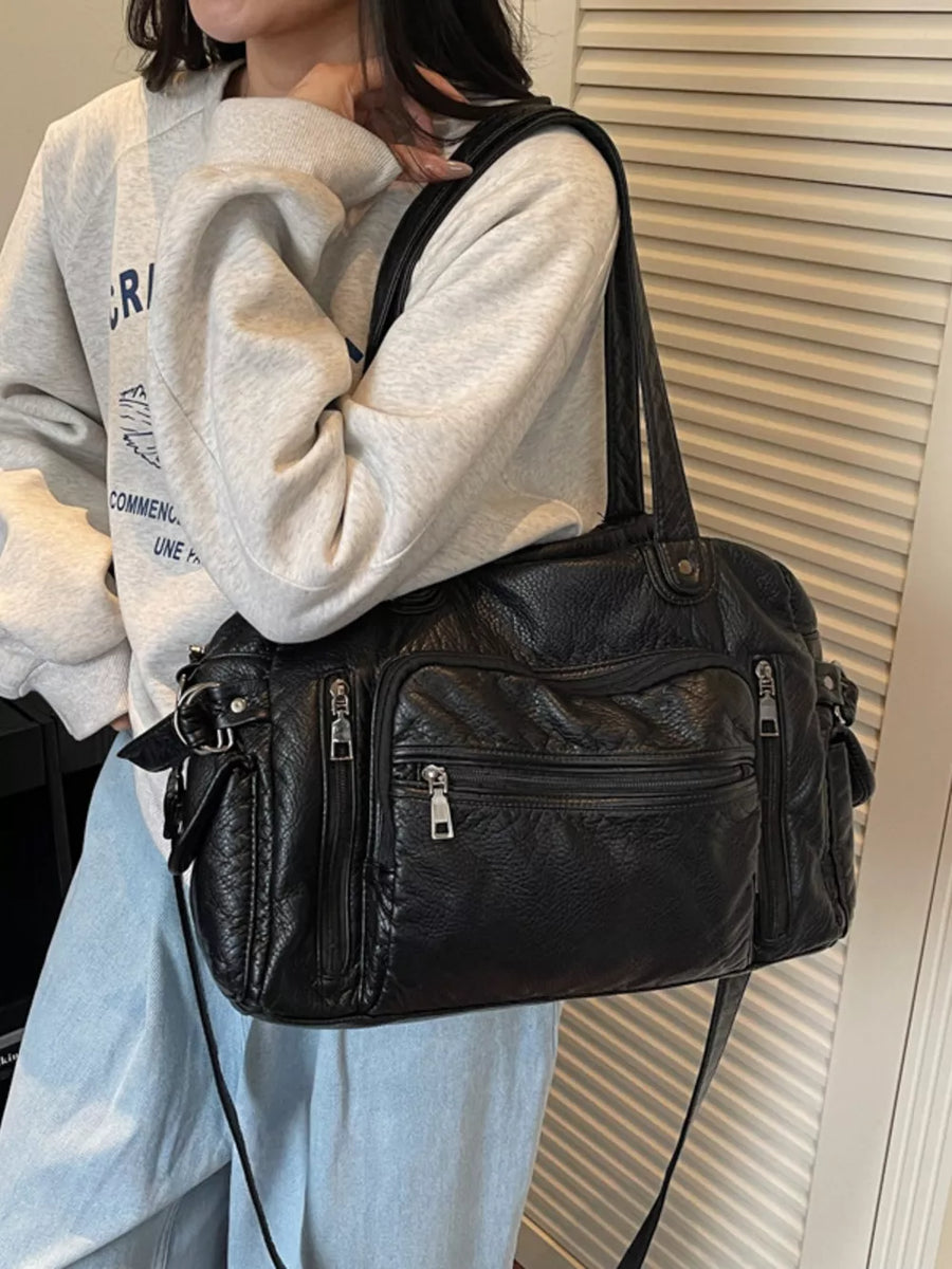 Black faux leather tote bag with multiple zippered pockets and silver hardware.