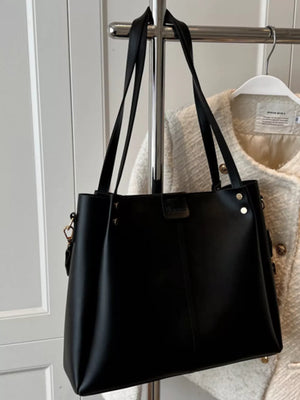 Black PU leather trapezoid handbag with wide straps and detachable strap detail.