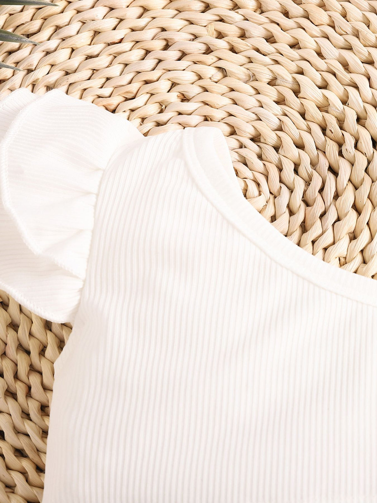 White ribbed cotton baby top with ruffled cap sleeves and asymmetrical neckline.