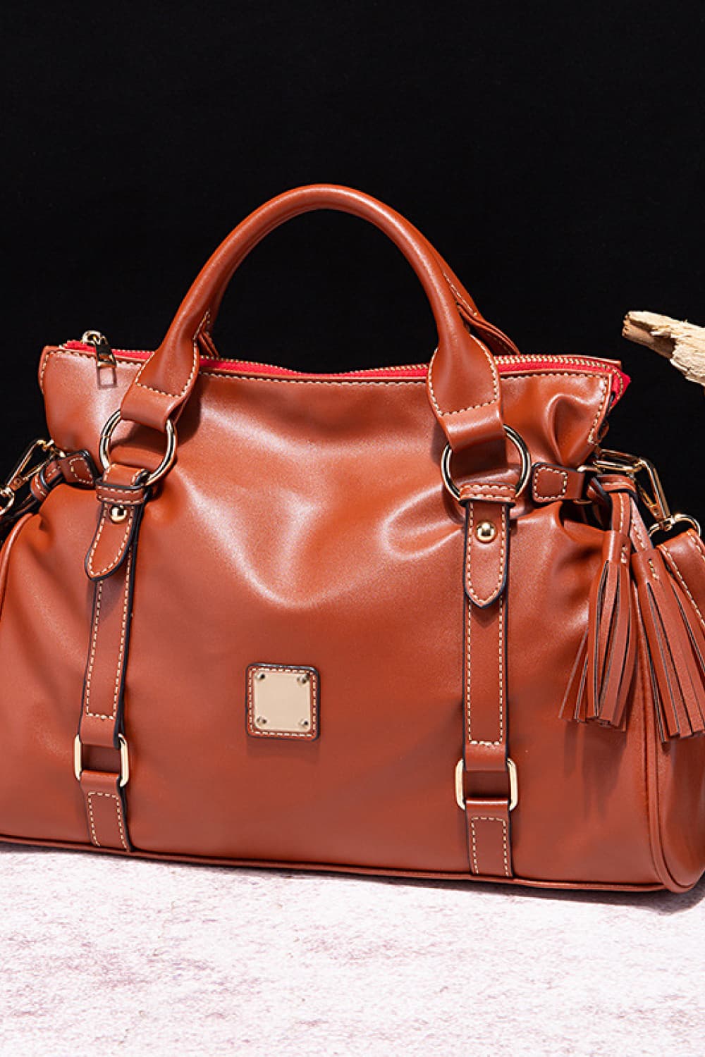 Structured satchel bag in caramel brown leather with tassel detail and gold hardware.