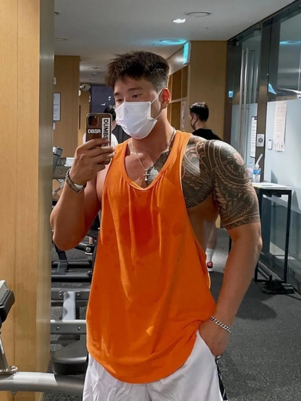 Orange scoop neck workout tank top with sweat stains, worn by a man with tattoos in a gym.