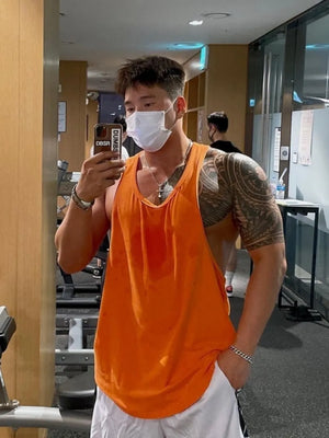Orange scoop neck workout tank top with sweat stains, worn by a man with tattoos in a gym.