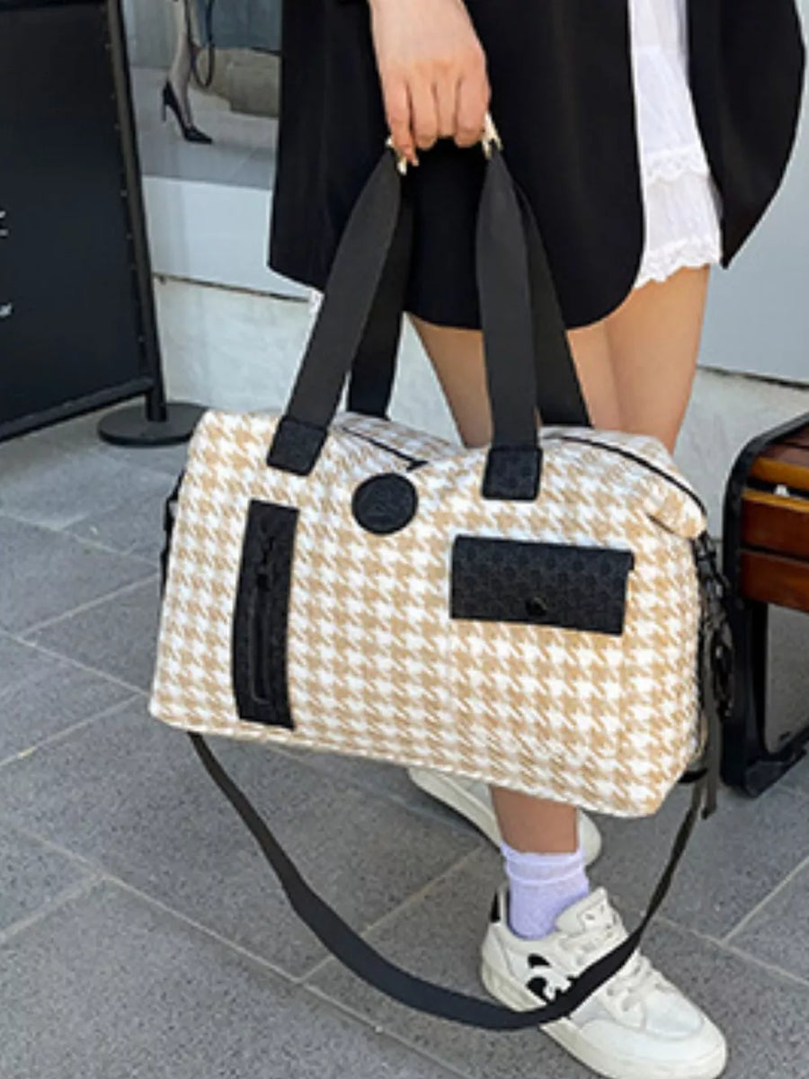 Chic houndstooth duffle bag with black accents and detachable strap.
