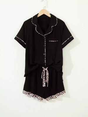 Black button-up pajama set with leopard trim on collar, cuffs, pocket, shorts tie and hem.