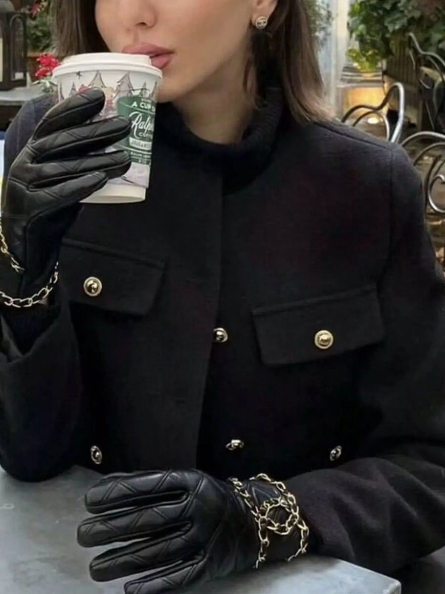 Black cropped tweed jacket with gold button details and chain accents on black leather gloves.