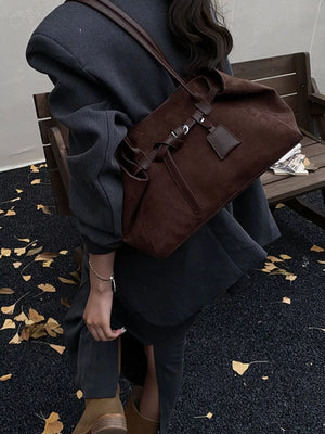 Brown suede shoulder bag with leather strap detail and a small tag.