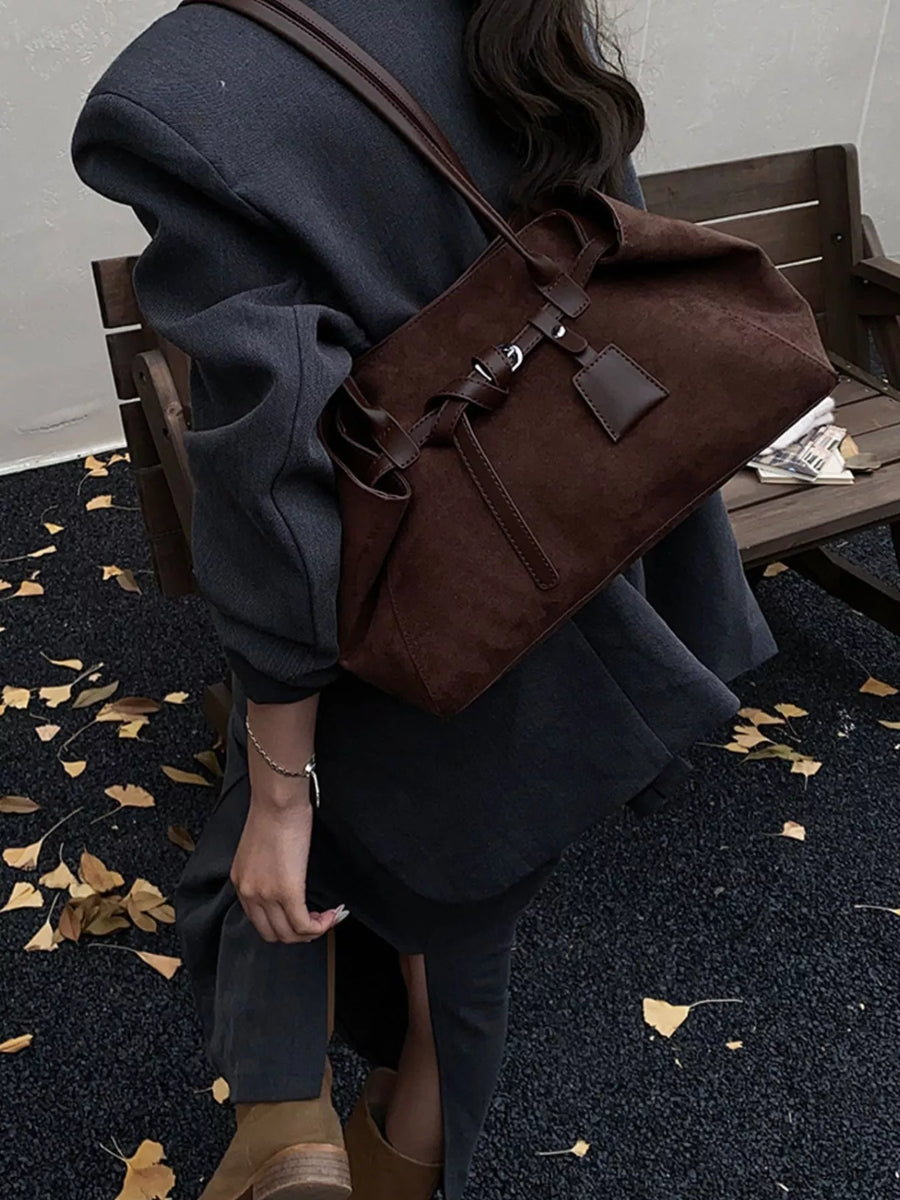 Brown suede shoulder bag with leather strap detail and a small tag.