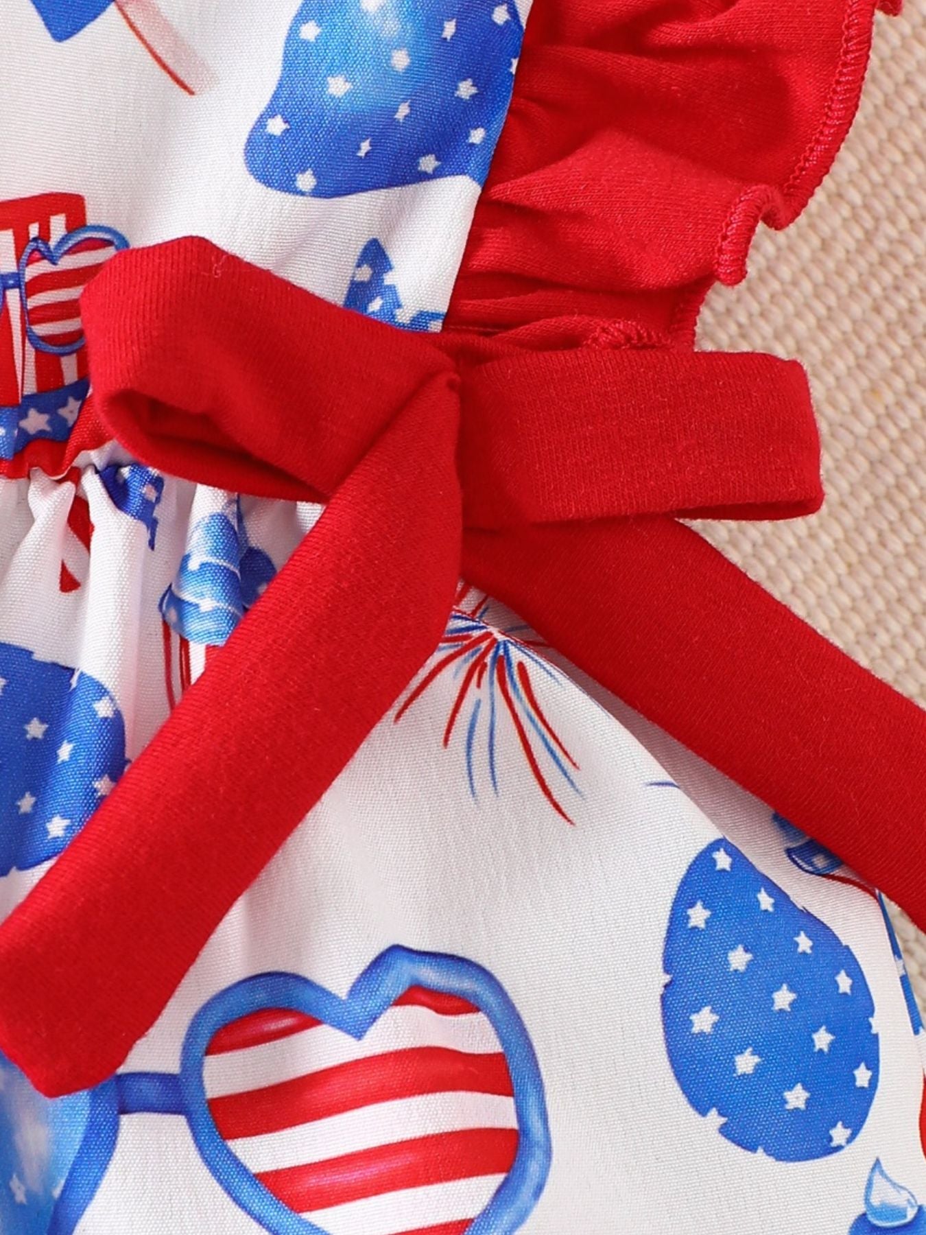 Baby one-piece with patriotic print, red ruffle sleeves, and a red bow detail.