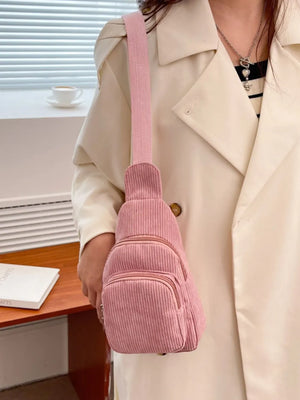 Pink corduroy sling bag with zip pockets worn by a person in a cream coat