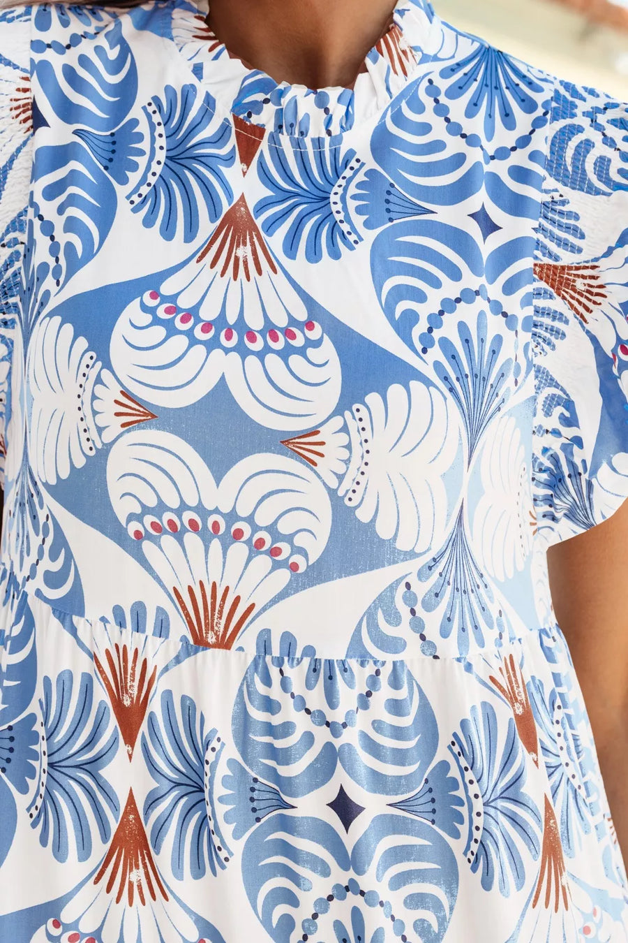 White and blue botanical print ruffled dress with flutter sleeves and tiered skirt detail.