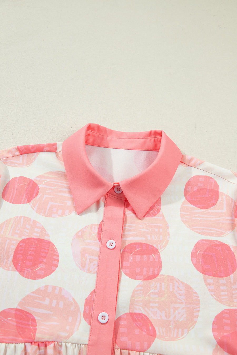Polka dot babydoll blouse with pink collar and button placket, ruffle trim detail.