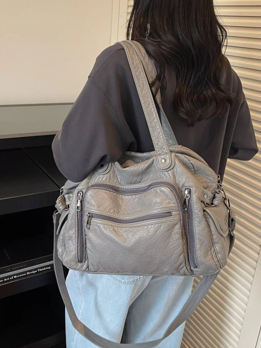 Grey leather crossbody bag with multiple zippered pockets and adjustable strap.