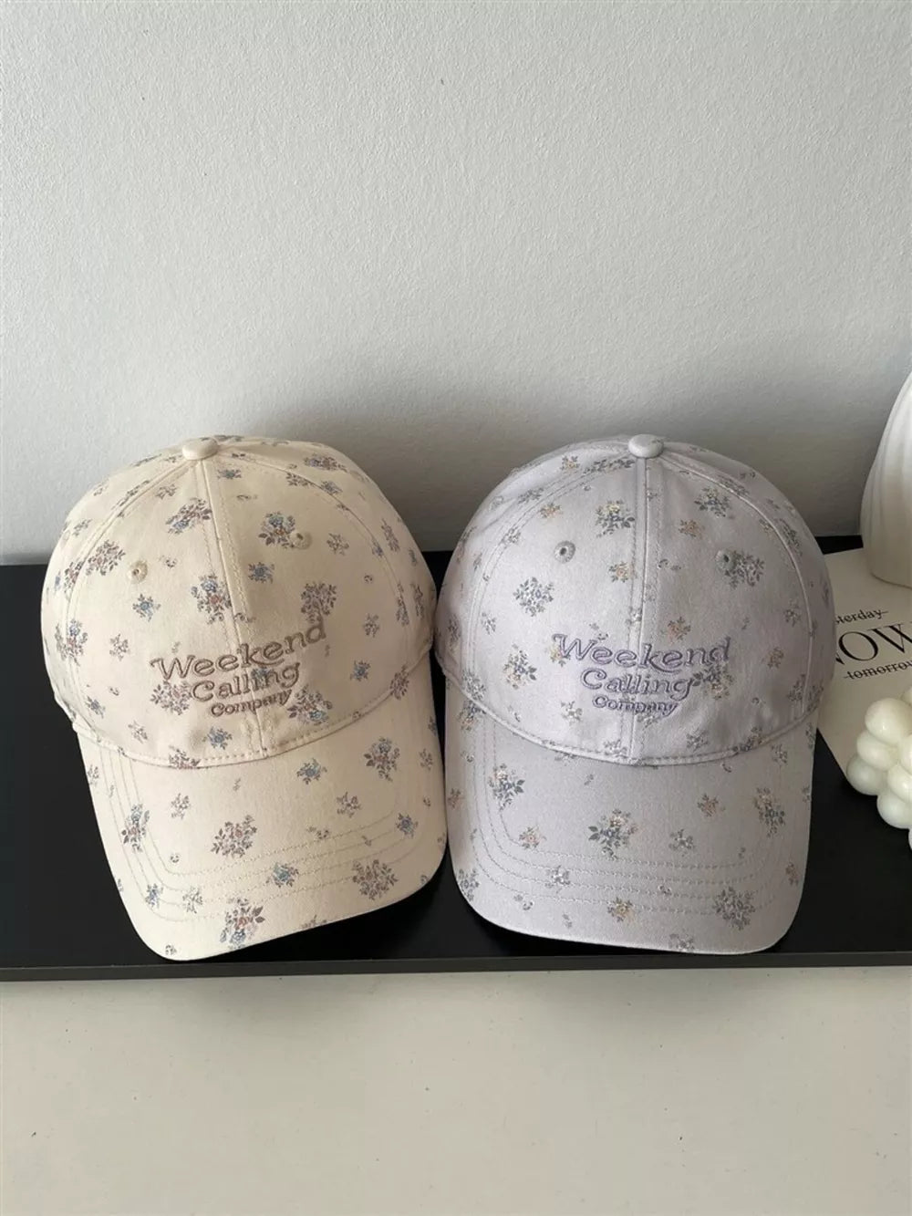Embroidered floral baseball caps in ivory and light gray with "Weekend Calling Company" text.