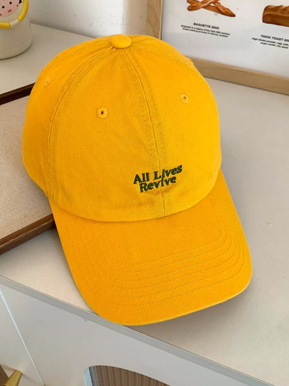 Yellow baseball cap with embroidered "All Lives Revive" text detail