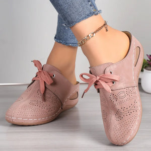 Dusty pink perforated lace-up mule flats with decorative cutouts and white stitching.