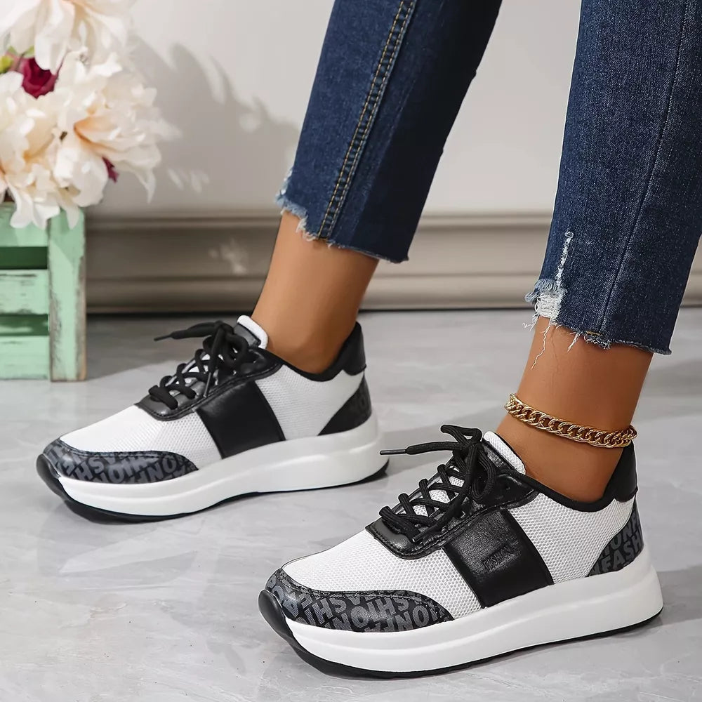 White and black lace-up sneakers with mesh and leather details and text print on the sole.