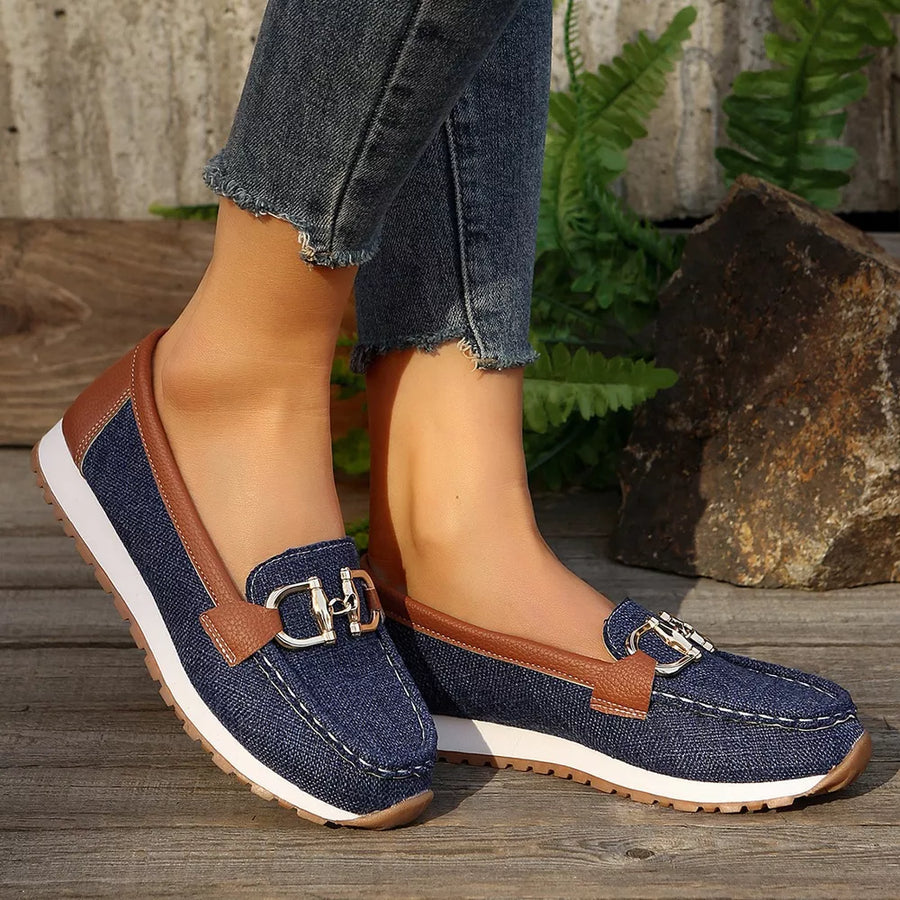 Blue denim round toe slip-on loafers with brown trim and silver buckle detail.