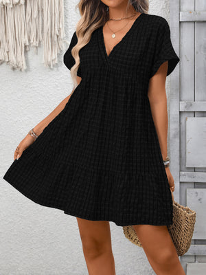 Black plaid V-neck mini dress with short sleeves and tiered hem.