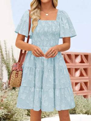 Light blue smocked mini dress with tiered skirt and floral texture.