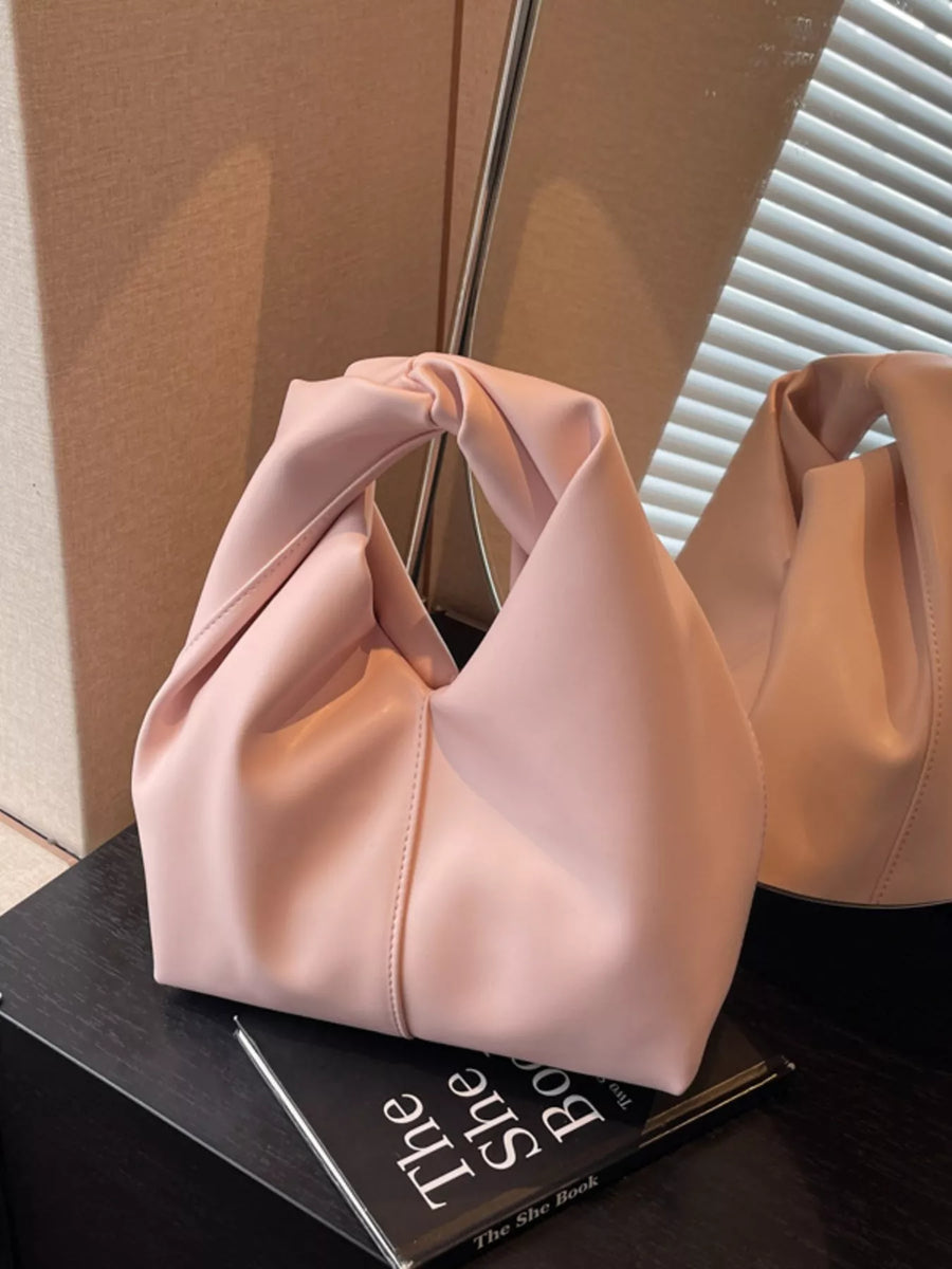 Blush pink leather handbag with a knotted handle and slouchy silhouette.