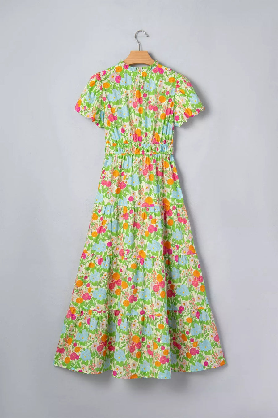 Maxi dress with short sleeves, ruffled neckline, tiered skirt, and a vibrant floral pattern in green, blue, pink, and orange.