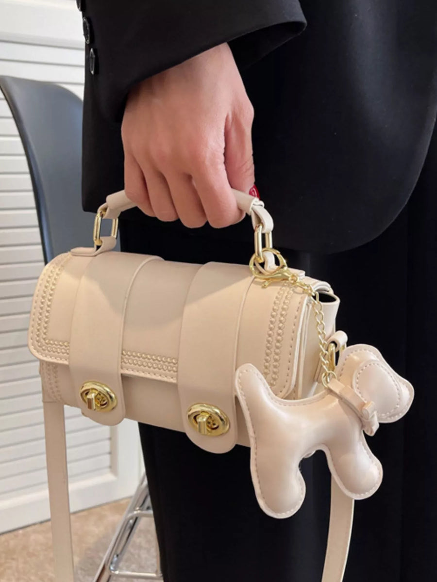 Mini beige PU leather crossbody bag with gold hardware and dog charm accessory.