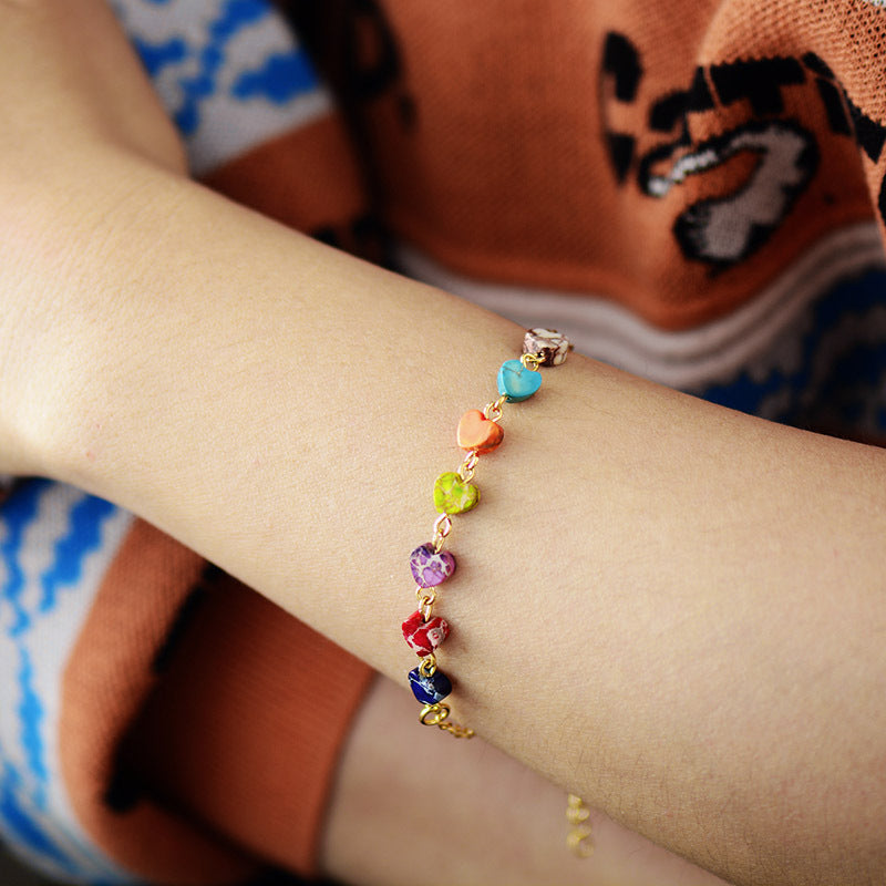 Multicolor heart stone bracelet with gold chain detail on a wrist.