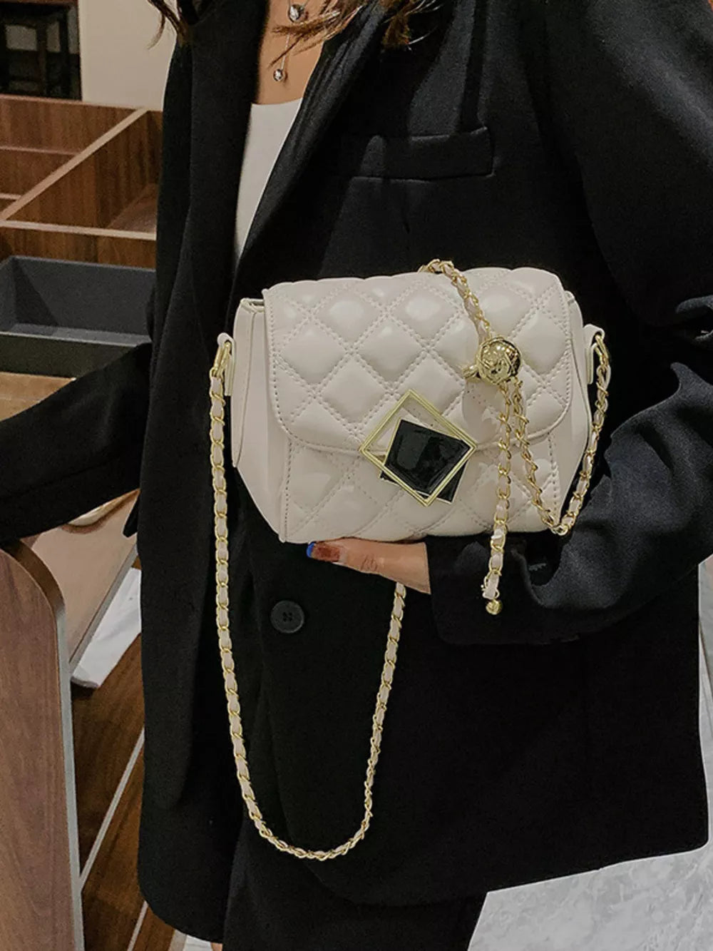 Elegant quilted crossbody bag in white with gold chain strap and geometric charm detail.