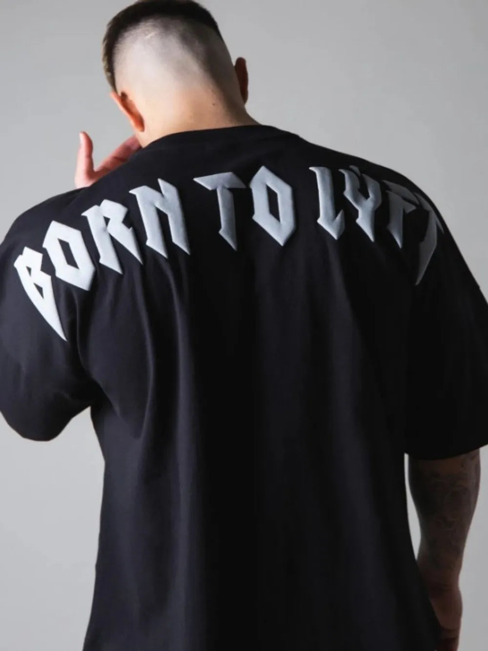 Black oversized graphic tee with white "BORN TO LY" text on back