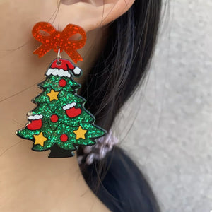 Festive Christmas tree dangle earrings with red bow, glitter green tree, red ornaments, yellow stars, and Santa hats.