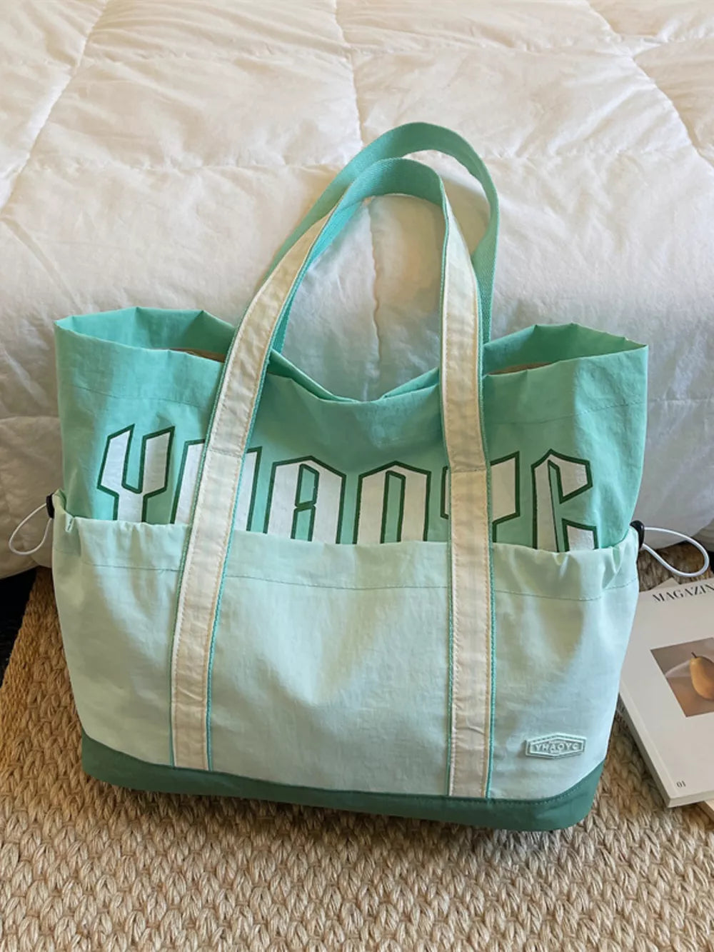 Green canvas drawstring shoulder bag with bold white lettering and dual straps.