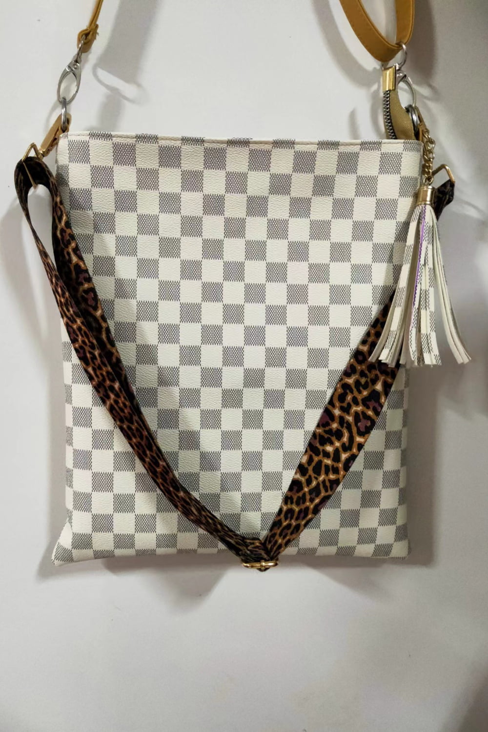 Cream crossbody bag with checkerboard pattern, leopard print strap, and tassel detail.