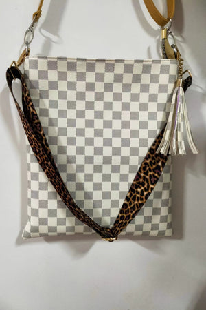 Cream crossbody bag with checkerboard pattern, leopard print strap, and tassel detail.