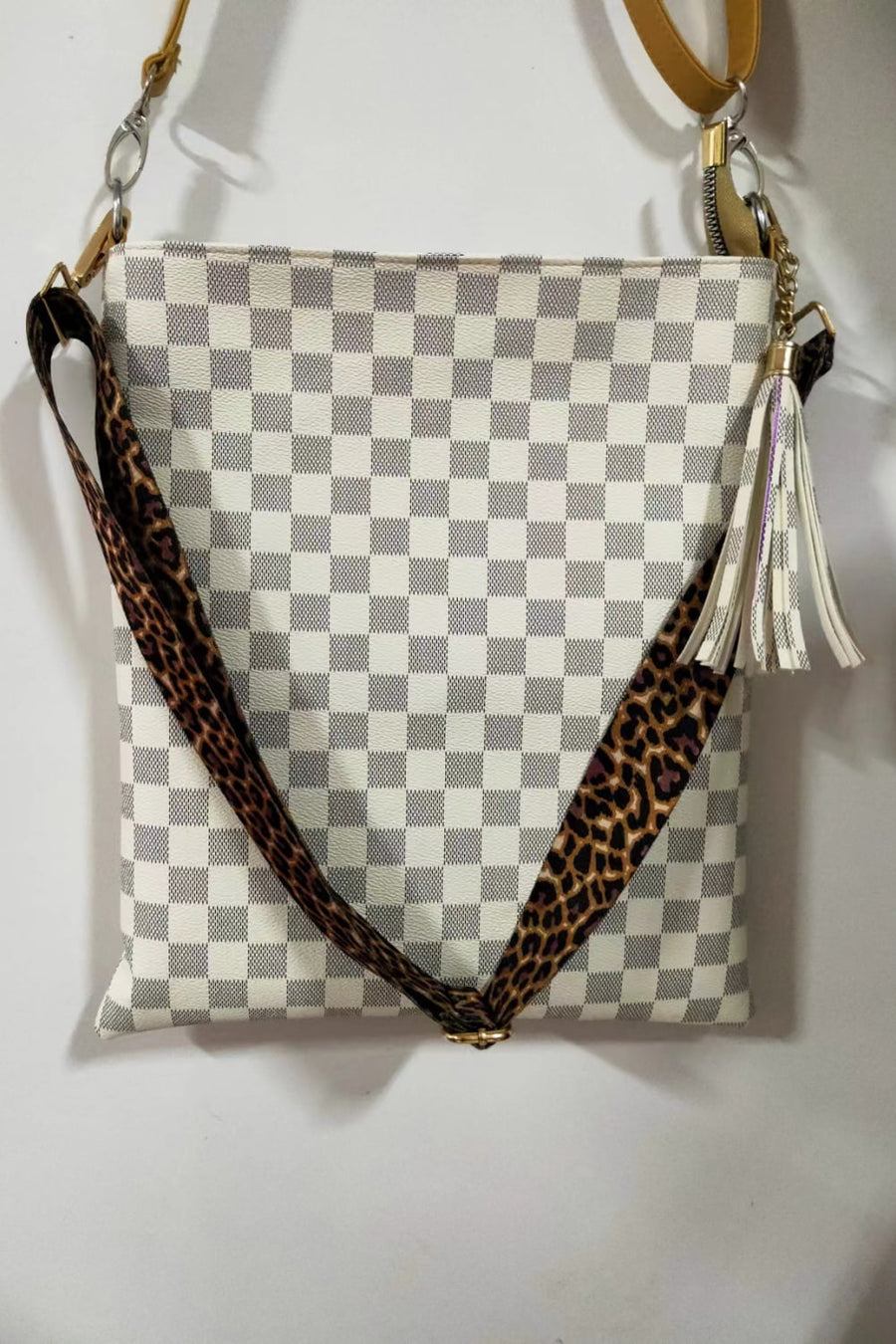 Cream crossbody bag with checkerboard pattern, leopard print strap, and tassel detail.