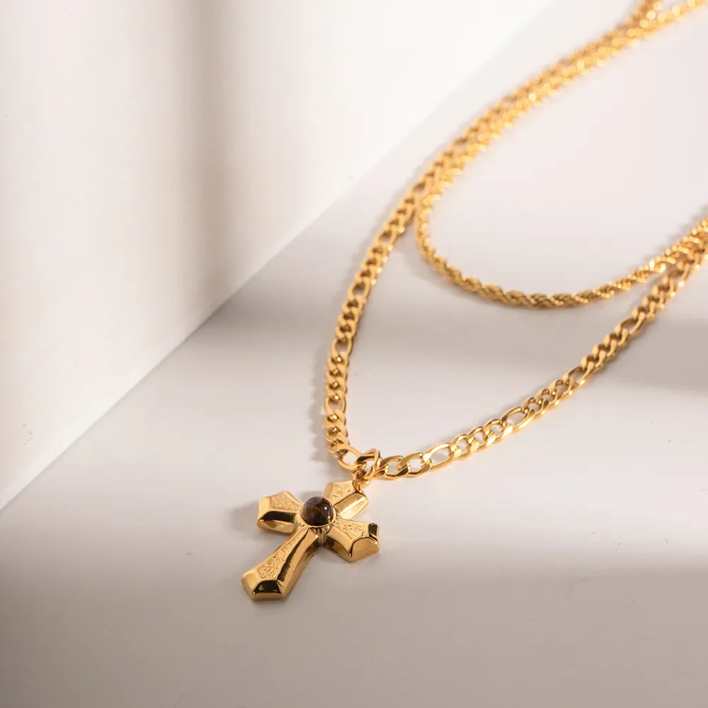 Gold layered chain necklace with a sculpted cross pendant featuring a dark stone accent.
