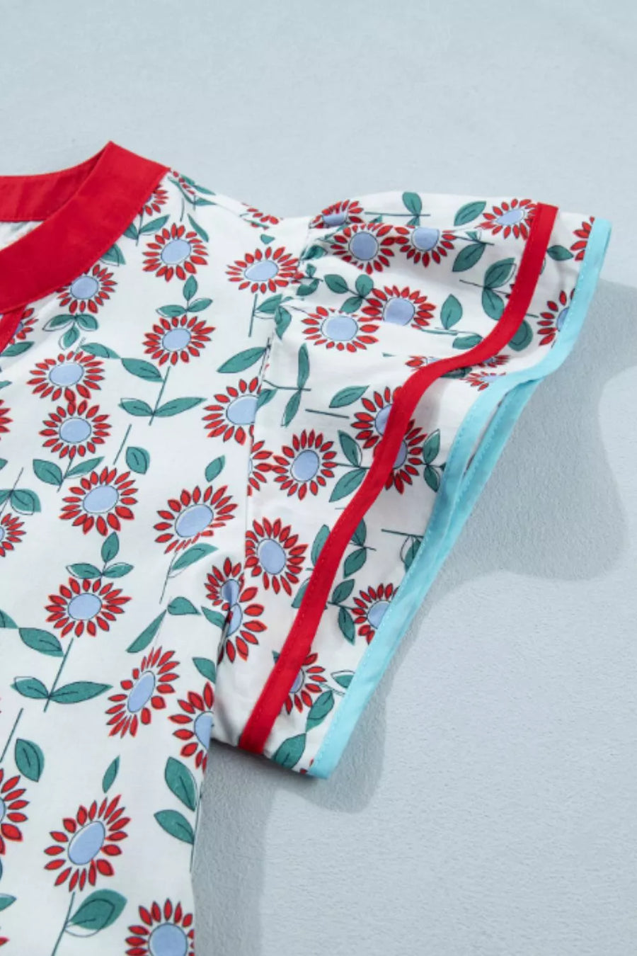 Cotton blouse with red and blue floral print, ruffle sleeves, and contrast trim.