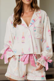 White silk pajama set with champagne print, collar, and pink bows on sleeves and shorts.