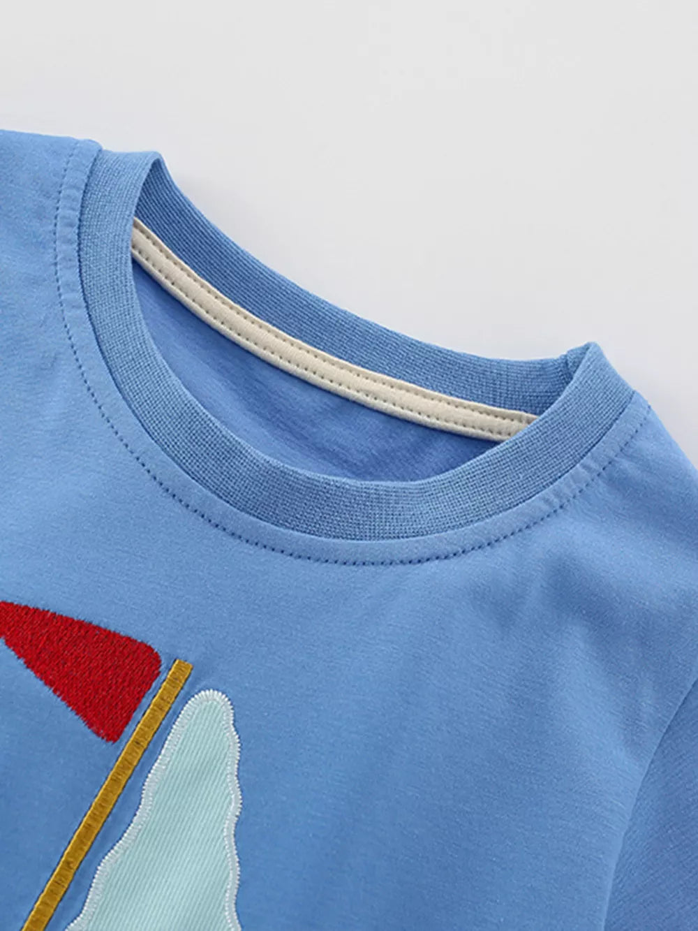 Blue cotton t-shirt with sailboat graphic and cream neck trim.