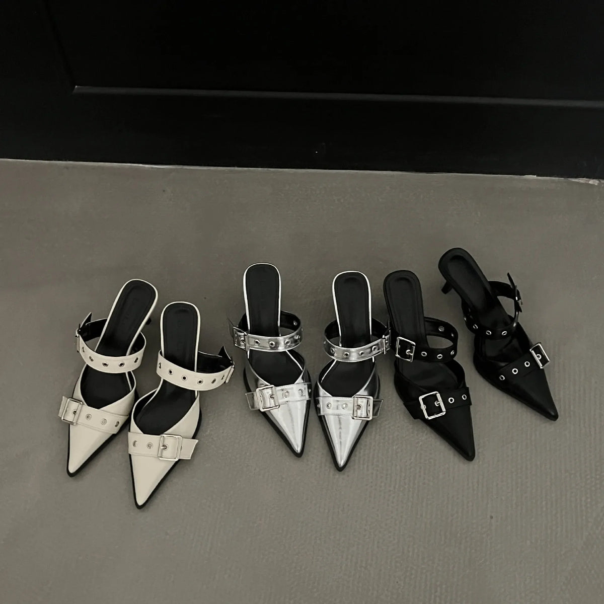 Metal pointed buckle mules in silver, beige, and black with strap details.