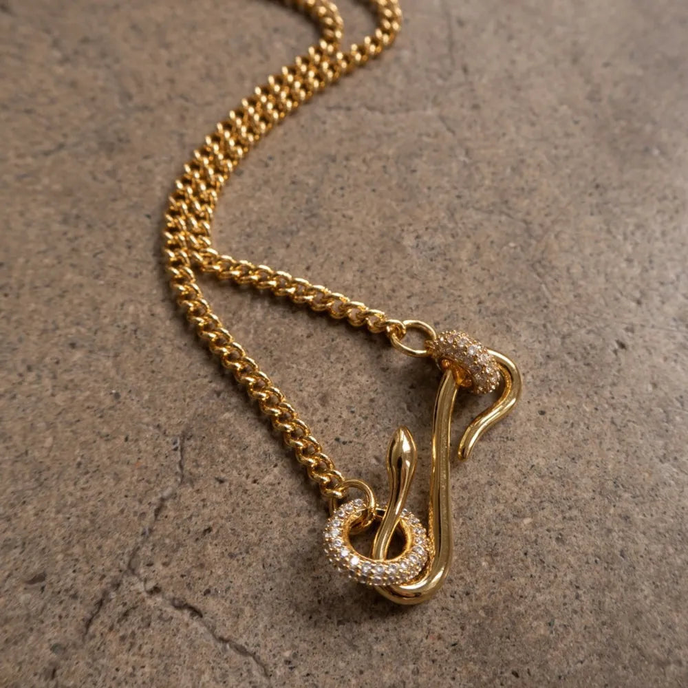 Gold curb chain necklace with a serpentine zirconia clasp and snake detail.