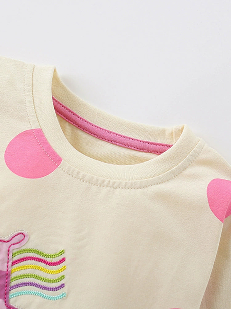 Cream cotton toddler pajama top with pink polka dots and rainbow embroidery detail.