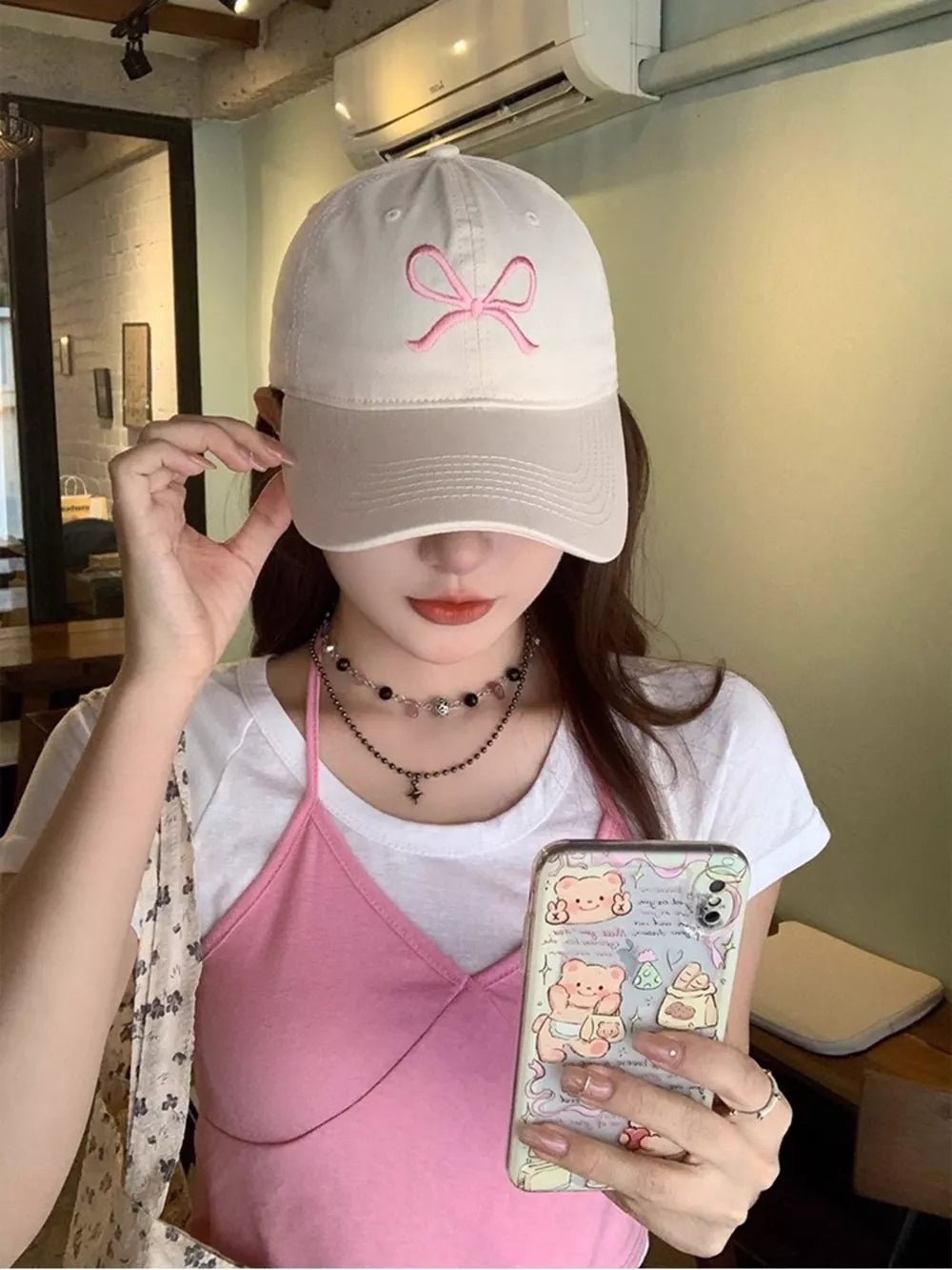 Baseball cap in cream and beige with pink bow embroidery, styled with a pink cami and white tee.