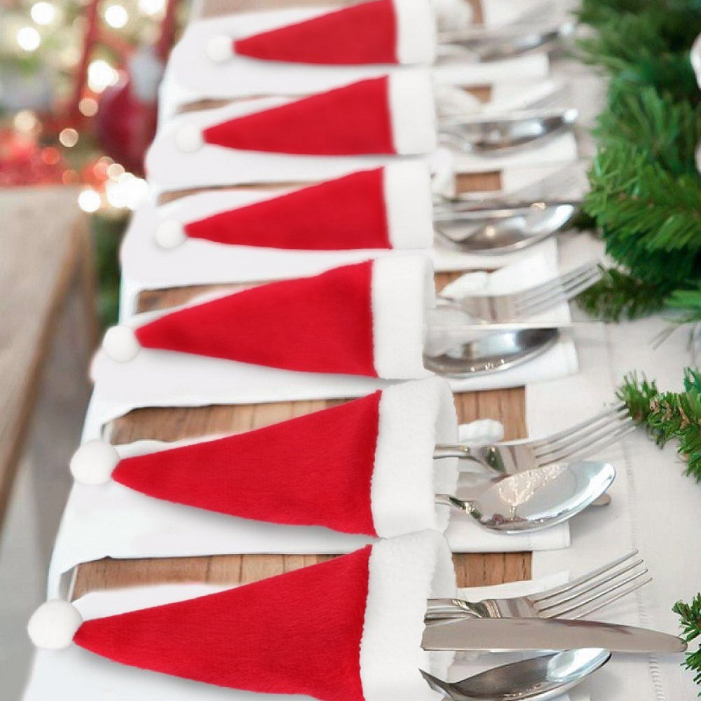 Red Santa hat cutlery holders with white trim and pom-poms, holding silverware on white napkins.