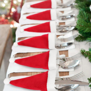 Red Santa hat cutlery holders with white trim and pom-poms, holding silverware on white napkins.