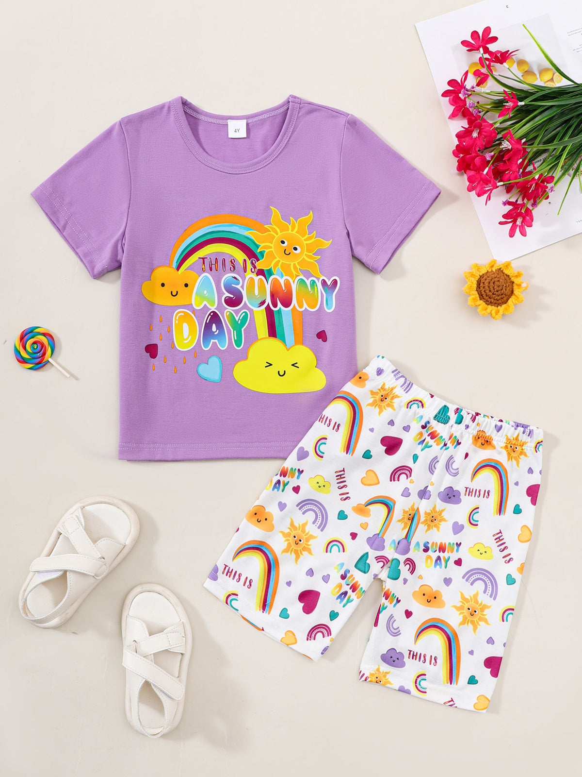 Girls' purple graphic tee and white printed shorts set with sun, rainbow, and cloud designs.