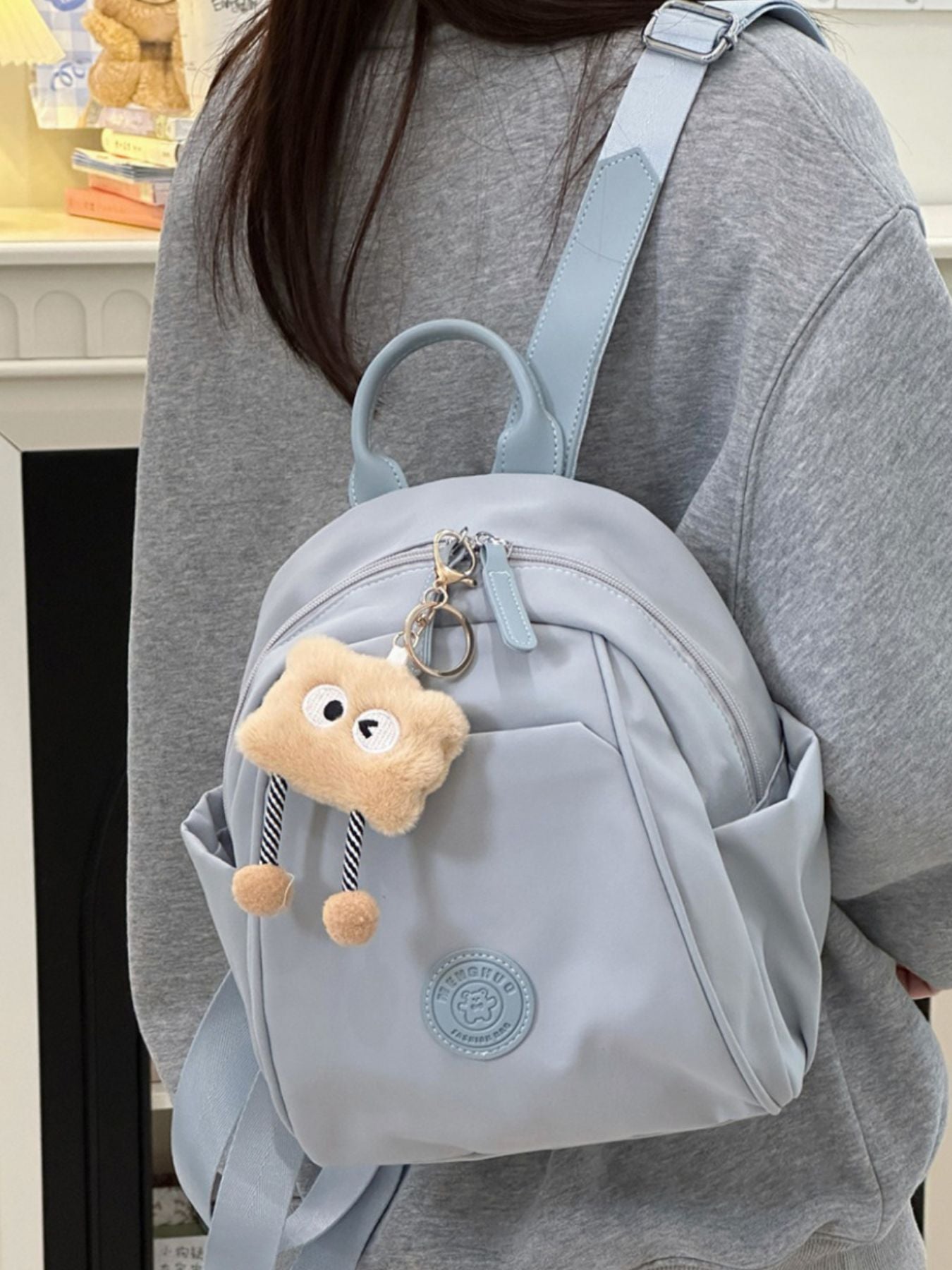 Mini nylon backpack in light blue with a fuzzy bear charm and zippered pockets.
